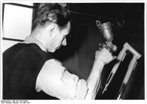Strahlenköpfe wurden mittels Schablonen per Hand gespritzt. Hier: "Der Speziallackierer und Aktivist Joachim Volkland der Fahrradwerke Mifa, Sangerhausen beim Spritzen von Strahlenköpfen." (1951)