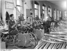 "In der Radspannerei. Nach dem Einhängen der Speichen werden diese gespannt, damit das Rad einen gleichmäßigen Lauf bekommt." (Juli 1956)