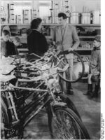 Fahrrädern im Konsum-Landwarenhaus Tambach-Dietharz (Thüringen) (Juni 1956). Ganz vorn steht ein Möve Modell 100. Es besitzt Sportradpedale sowie einen Scheinwerfer, die nach herkömmlicher Art mit einem Halter am Schaft des Vorbaulenkers befestigt ist. Die Schutzbleche scheinen in der Rahemenfarbe lackiert zu sein. Die hier angebrachten Fahrradgriffe sind bislang nicht bekannt.