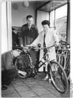 "Durch die Preissenkung erhält Frau Erika Fehrmann ihr Fahrrad eher als sie dachte. In der HO-Fahrzeughalle in der Stalinallee, Berlin, sucht sie sich zusammen mit ihrem Manne ein Fahrrad aus. Dieses Fahrrad kostete 341,50 DM. Neuer Preis! 261.- DM" (Juni 1956)