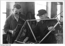 "Meister Schmidt, der seine Norm um 33 % erhöht hat, schweißt den Vorder- und Hinterbau eines Fahrrades zusammen." (1949)