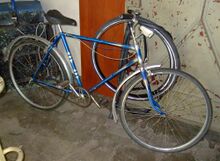 Fahrrad der Marke Brandenburg, lackiert von der Lackiererei Lindenkreuz. Charakteristisch sind der blaue Metallic-Lack, die weiße Kastenlinierung, das silberne Ringdekor am Sitzrohr sowie der orange eingefasste Strahlenkopf mit silbernem Farbverlauf. Die Lackiererei Lindenkreuz lackierte viele Fahrräder in diesem Stil.