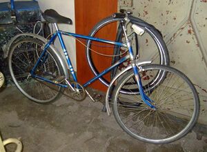 Brandenburg-Fahrrad, lackiert von der Lackiererei Lindenkreuz. Charakteristisch sind der blaue Metallic-Lack, die weiße Kastenlinierung, das silberne Ringdekor am Sitzrohr sowie der orange eingefasste Strahlenkopf mit silbernem Farbverlauf. Die Lackiererei Lindenkreuz lackierte viele Fahrräder in diesem Stil.