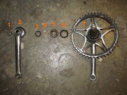 9. Übersicht der ausgebauten Teile Das Bild zeigt die Teile in der Reihenfolge, in der sie demontiert wurden: 1 - Sicherungsmutter der Kurbel; 2 - linke Kurbel; 3 - Sicherungsmutter des Konus'; 4 - Nasenscheibe (Verdrehsicherung); 5 - linker Konus; 6 - linker Kugelring; 7 - Einheit aus rechter Kurbel mit Kettenblatt, Tretlagerwelle und rechtem Konus samt Kugelring