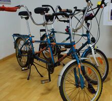 Prototyp des Tandems mit der Bezeichnung "WEEKEND TOURING". Im Hintergrund ein nach 1990 gebautes Exemplar. Auffällig sind der Hinterbau des Rahmens (ähnlich dem des BMX-Fahrrades ausgeführt) und die starre Vorderradgabel, ebenfalls wie beim BMX-Fahrrad. Einige Teile (u. a. Tretlager, Schaltwerk) an diesem Fahrrad sind nicht aus DDR-Produktion.