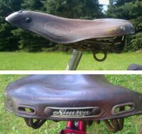 Sportsattel von ?? Zeitraum: 195? bis 1957 Verwendung: Zubehörteil für Simson-Fahrräder Lederdecke: braun lackiert Gestell: verchromt Bemerkungen: lange Ausführung, Gestell mit zusätzlichen Federschleifen, mit Simson-Plakette aus Kunststoff an der Rückseite, länger als Möve-Sportsättel, Hersteller unbekannt